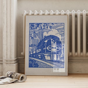 May include: Blue and white vintage-style print of a Santa Fe train, set against a backdrop of city buildings and clouds. The artwork is framed and leans against a wall, evoking a sense of nostalgia and travel.