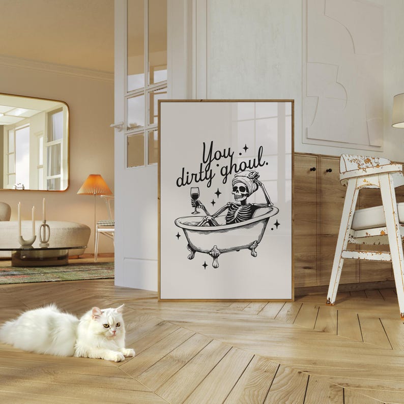 Funny Halloween decor. Light beige background with black foreground. Illustration of a skeleton sitting in a vintage bathtub with a glass of wine and text that reads you dirty ghoul. Perfect bathroom decor for the fall autumn season.
