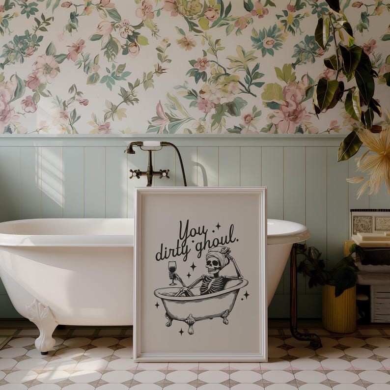 Funny Halloween decor. Light beige background with black foreground. Illustration of a skeleton sitting in a vintage bathtub with a glass of wine and text that reads you dirty ghoul. Perfect bathroom decor for the fall autumn season.