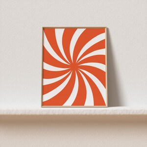 Op de afbeelding: Een ingelijst print met een swirlend oranje en wit patroon. De print is in een eenvoudige houten lijst.