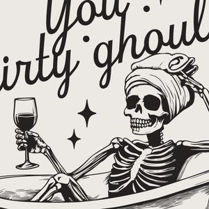 Funny Halloween decor. Light beige background with black foreground. Illustration of a skeleton sitting in a vintage bathtub with a glass of wine and text that reads you dirty ghoul. Perfect bathroom decor for the fall autumn season.