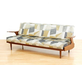 May include: Mid-century modern sofa with a geometric patterned fabric in shades of gray, yellow, and beige. The sofa has a wooden frame, armrests, and tapered legs. The sofa is approximately 78 inches long.