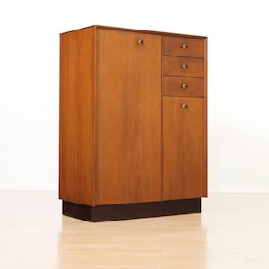 May include: A tall wooden cabinet with a light brown wood grain finish, featuring one large door on the left and a column of three small drawers above a single smaller door on the right, all accented with small, round, dark-colored knobs.