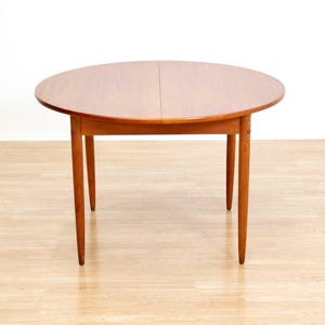 May include: A round wooden dining table with a light brown finish. The table has four tapered legs and a split tabletop. The table is approximately 48 inches in diameter.