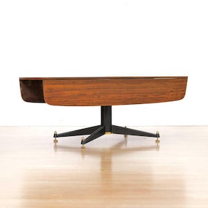 May include: A mid-century modern coffee table with a dark wood grain top and a black, starburst-style base. The base has brass-colored accents on the feet. The table is set against a white background.