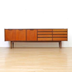 May include: A mid-century modern wooden sideboard with a warm, reddish-brown finish. The cabinet features three doors on the left, a set of drawers on the right, and a long, rectangular shape. It stands on four tapered legs.