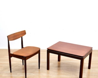 May include: A mid-century modern teak wood table and chair set. The table has a rectangular top and four legs. The chair has a brown leather seat and a back with a curved top.