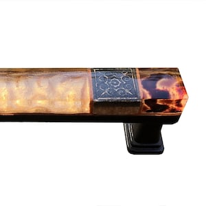 May include: A rectangular glass door handle with a black metal base. The glass is multi-colored with a brown, orange, and yellow pattern. The glass is also decorated with a black and gold floral design.