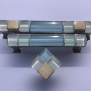 May include: Two blue and beige mosaic glass cabinet pulls and a matching knob. The pulls are rectangular and the knob is square.