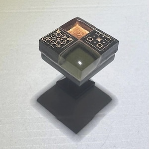 May include: Square ceramic cabinet knob with a geometric design in black, brown, and green with gold accents.