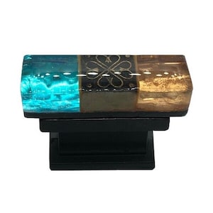 May include: A rectangular glass cabinet knob with a turquoise, black, and gold design. The knob is mounted on a black base.