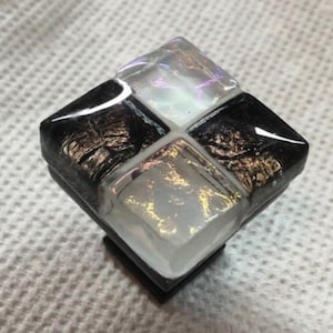 May include: Square glass cabinet knob with a black and white mosaic design. The glass has a iridescent finish with gold flecks.