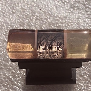 May include: A brown, black, and gold glass cabinet knob with a black base. The glass is clear and has a textured surface. The knob has a rectangular shape.