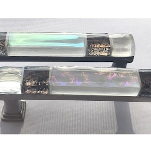 May include: Two glass cabinet door pulls with a black and silver finish. The glass is clear with iridescent accents and a black metallic stripe.