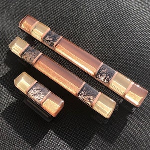 May include: Three glass cabinet knobs in different sizes. The knobs are made of layered glass with a copper, gold, and black design.