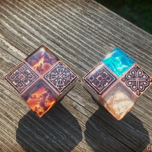 May include: Two square-shaped decorative tiles with a geometric pattern. One tile has a blue center and the other has an orange center. Both tiles have a brown and white geometric pattern around the center.