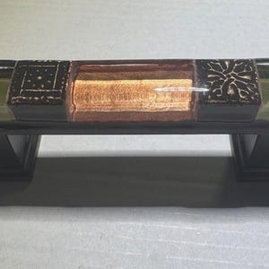 May include: A decorative cabinet pull with a brown, green, and orange design. The pull is made of ceramic and has a rectangular shape.