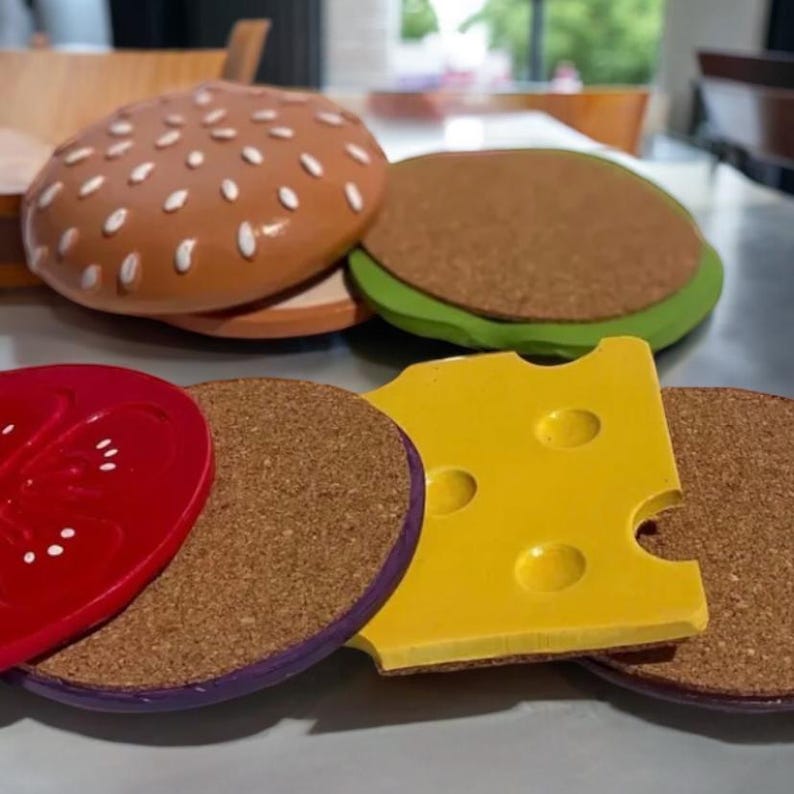 May include: A set of five toy food items, including a hamburger, a green lettuce bun, a red tomato slice, a yellow cheese slice, and a brown bun. The items are made of felt and are designed to look like real food.