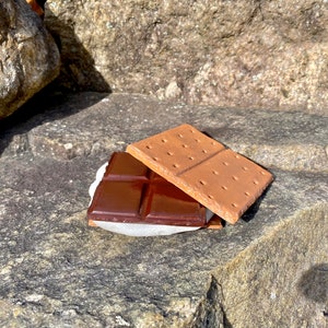 K&ouml;nnte beinhalten: Ein S'more mit einem Graham-Cracker, einem Schokoriegel und einer Marshmallow auf einem Stein.