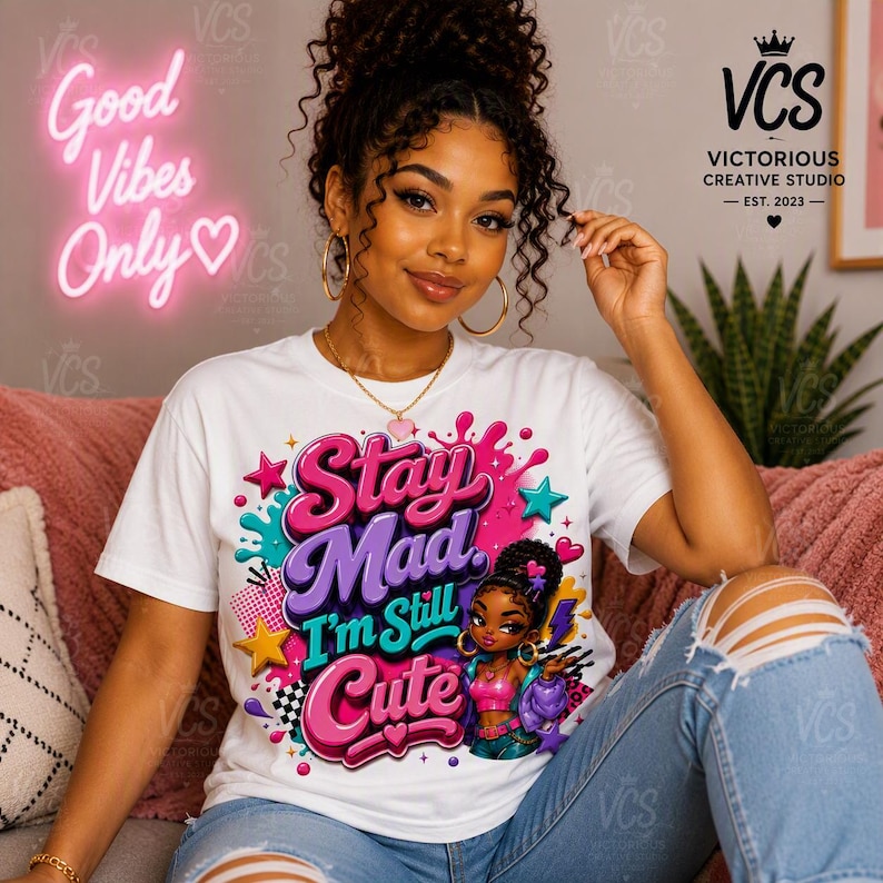 K&ouml;nnte beinhalten: Ein wei&szlig;es kurz&auml;rmeliges T-Shirt mit einem farbenfrohen Grafikdruck und dem Text Stay Mad I'm Still Cute. Das Design zeigt eine Zeichentrickfigur, rosa und lila Schriftz&uuml;ge, Sterne und Farbspritzer. Das Shirt hat einen Rundhalsausschnitt.