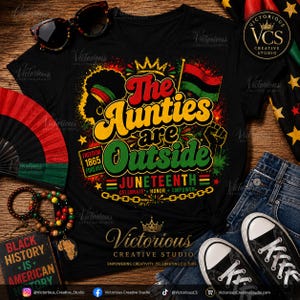 Op de afbeelding: Zwart T-shirt met de tekst "The Aunties are Outside" in geel, groen en rood, ter viering van Juneteenth. Voorzien van een silhouet, vlag en vuistafbeelding. Accessoires: zonnebril, armbanden en een waaier.