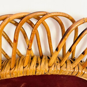 May include: Close-up of a vintage rattan chair back. The chair back features a woven base with a deep red cushion and arched rattan supports. The rattan is a light brown color with darker accents, creating a natural, textured look.