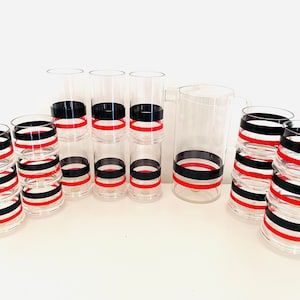 May include: Set of clear acrylic glasses and a pitcher with black and red stripes. The glasses are stacked in groups of three and the pitcher is on its own.