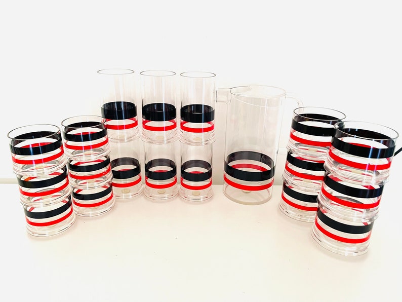 May include: Set of clear acrylic glasses and a pitcher with black and red stripes. The glasses are stacked in groups of three and the pitcher is on its own.