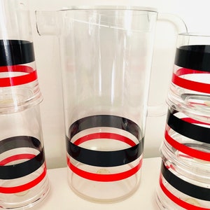 May include: A set of clear glass pitcher and glasses with black and red stripes. The pitcher has a handle and the glasses are stacked.