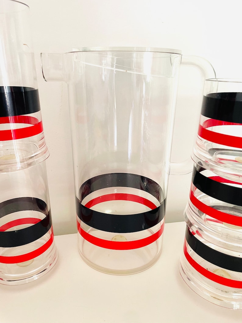 May include: A set of clear glass pitcher and glasses with black and red stripes. The pitcher has a handle and the glasses are stacked.