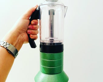 Pode incluir: Uma cafeteira de vidro transparente e verde com uma pega preta e uma base verde.