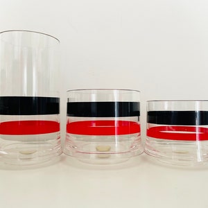 May include: Three clear glass tumblers with black and red bands. The tumblers are different sizes and are arranged from largest to smallest.
