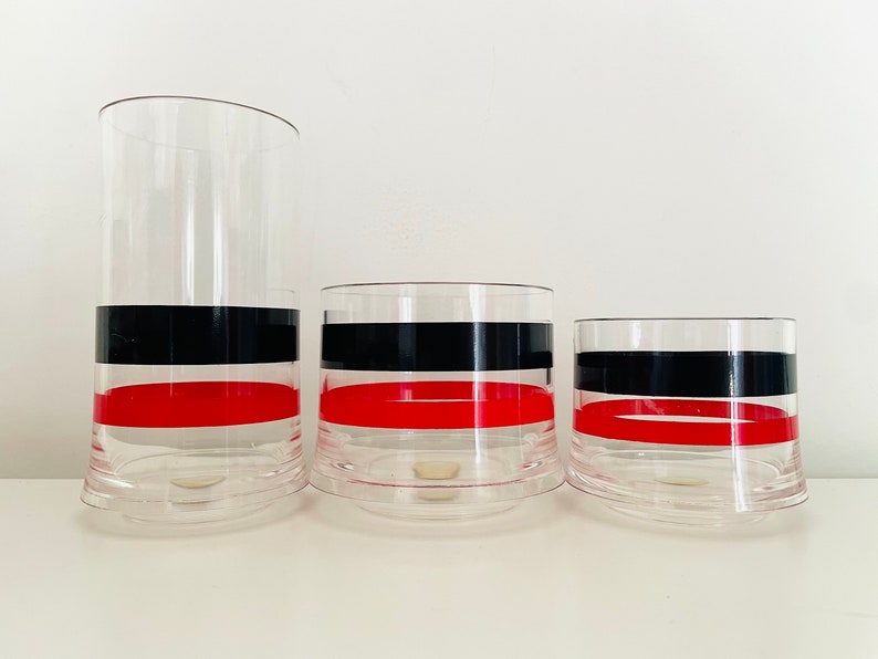 May include: Three clear glass tumblers with black and red bands. The tumblers are different sizes and are arranged from largest to smallest.
