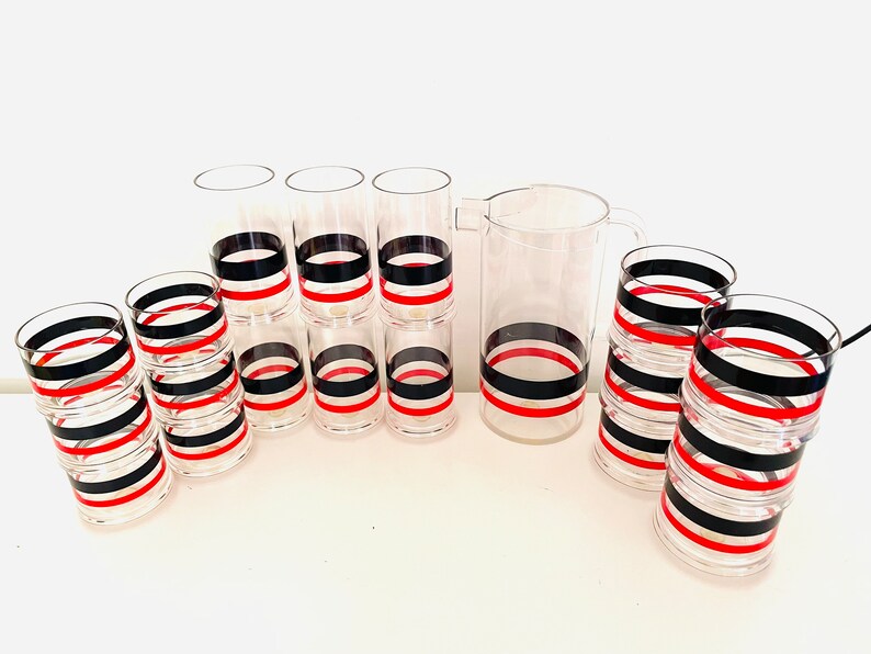 May include: Set of clear glass tumblers and a pitcher with black and red striped designs.