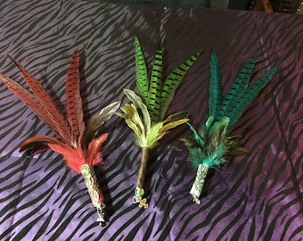 May include: Three feather wands with different coloured feathers. The wands are decorated with beads and charms. The feathers are red, green and blue.