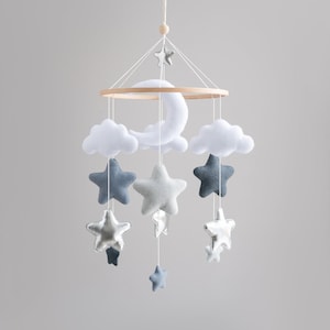 May include: A white and gray baby mobile with a crescent moon, clouds, and stars. The mobile is made of felt and has a wooden ring.