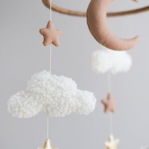 Op de afbeelding: Een mobiel met een witte, pluche wolk, een bruine vilt halve maan en gouden en bruine vilt sterren die aan een houten ring hangen. Deze mobiel is perfect voor een babykamer.