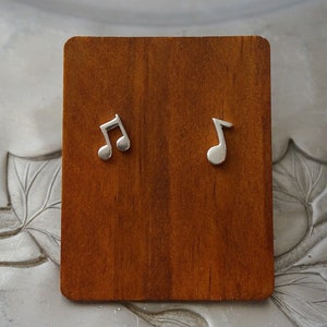 May include: A pair of silver musical note earrings on a wooden display stand.