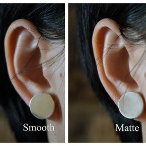 May include: Close-up of a person's ear with two silver earrings. The earring on the left is smooth and the earring on the right is matte.