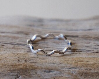 May include: A silver ring with a wavy design. The ring is on a piece of driftwood.