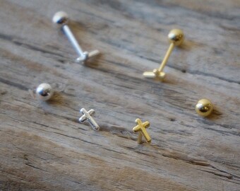 May include: Four silver and gold stud earrings with a cross and ball design. The earrings are displayed on a wooden surface.
