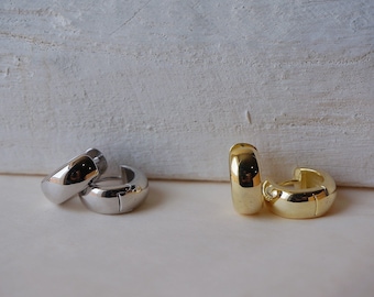 May include: Two pairs of hoop earrings, one pair is silver and the other is gold. The earrings are on a white surface.