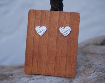 May include: A pair of silver heart-shaped earrings on a wooden display stand.