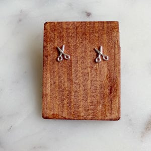 May include: A pair of silver scissor earrings on a wooden display stand.