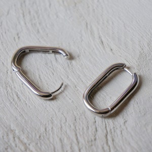 May include: A pair of silver hoop earrings with a rectangular shape. The earrings are made of a smooth metal and have a simple design.