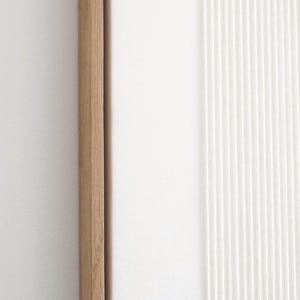May include: A close-up of a modern wall art piece. The artwork features a natural wood frame, a smooth white surface, and a textured white section with vertical lines. The design is minimalist and contemporary.