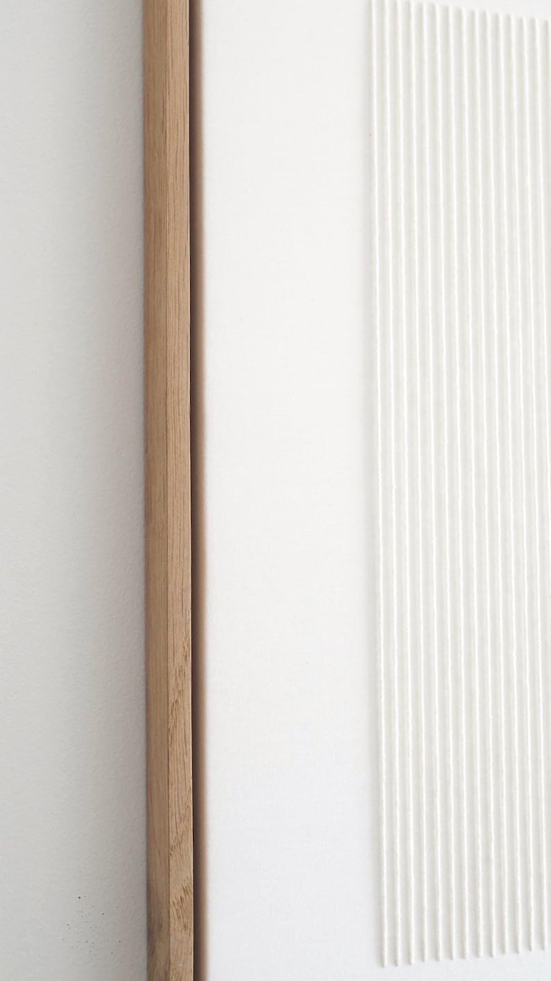 May include: A close-up of a modern wall art piece. The artwork features a natural wood frame, a smooth white surface, and a textured white section with vertical lines. The design is minimalist and contemporary.