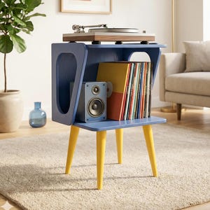 May include: A blue and yellow record player stand with a turntable, speaker, and vinyl records. The stand has a mid-century modern design with yellow legs and a blue body. The stand is in a living room setting. The stand measures approximately 76 cm in height.