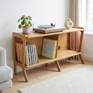 May include: A wooden record player stand with a turntable, records, and a small potted plant. The stand has a natural wood finish and a mid-century modern design. A white vase sits on the stand. A framed landscape painting hangs on the wall.