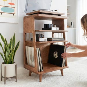 May include: A wooden record player stand with four tapered legs, featuring a top surface for a turntable, two middle shelves for audio equipment, and a bottom section with vertical string dividers for organising vinyl record albums.